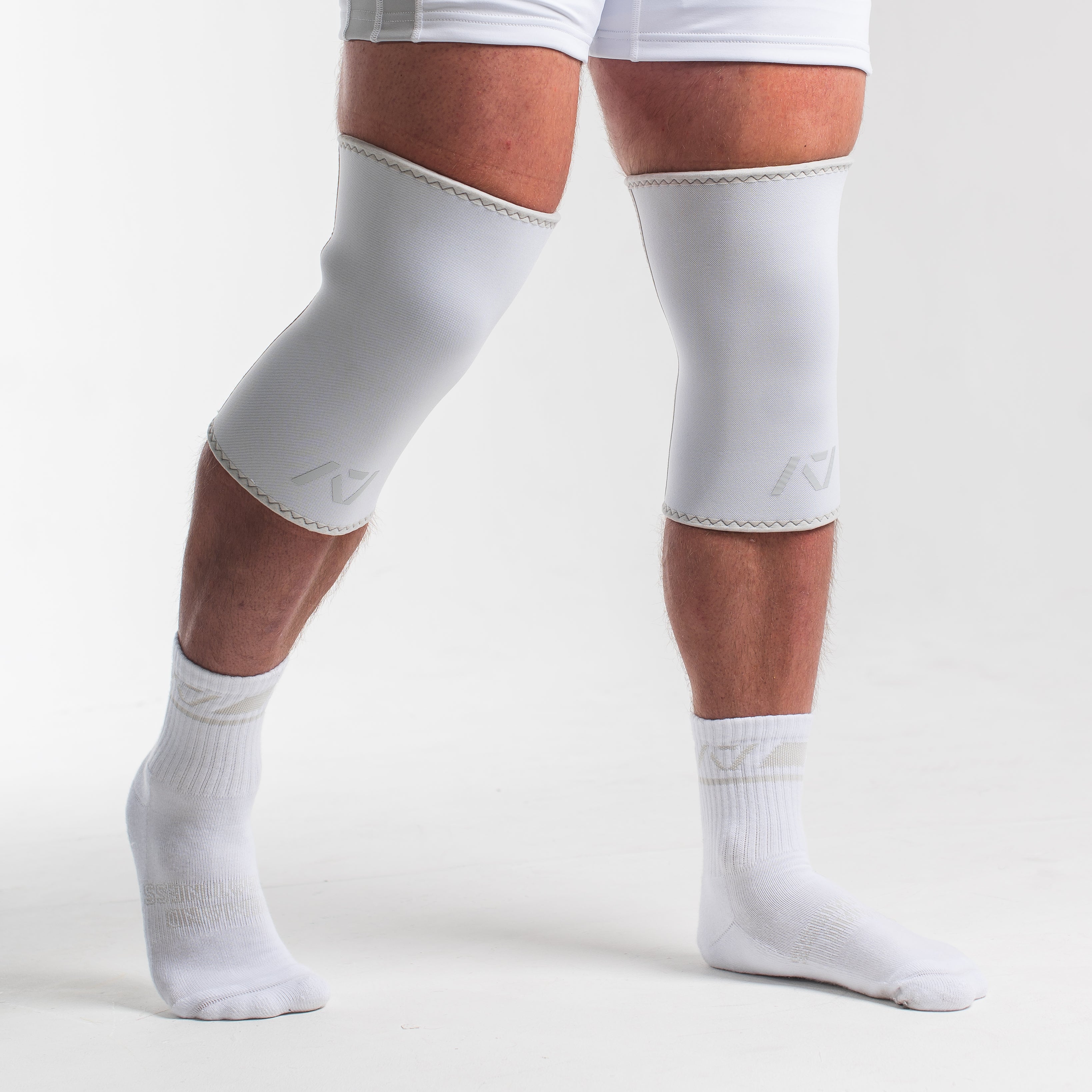 Person wearing white knee sleeves and singlet on a plain background