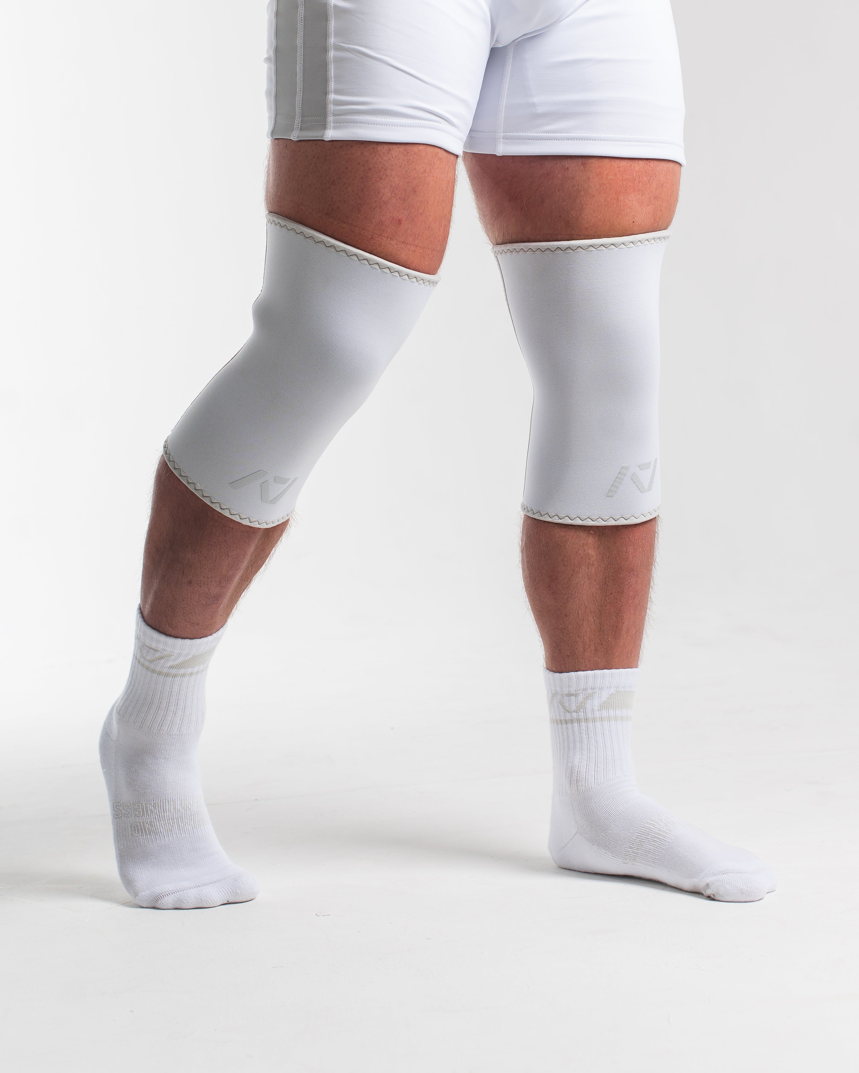 Person wearing white knee sleeves and singlet on a plain background