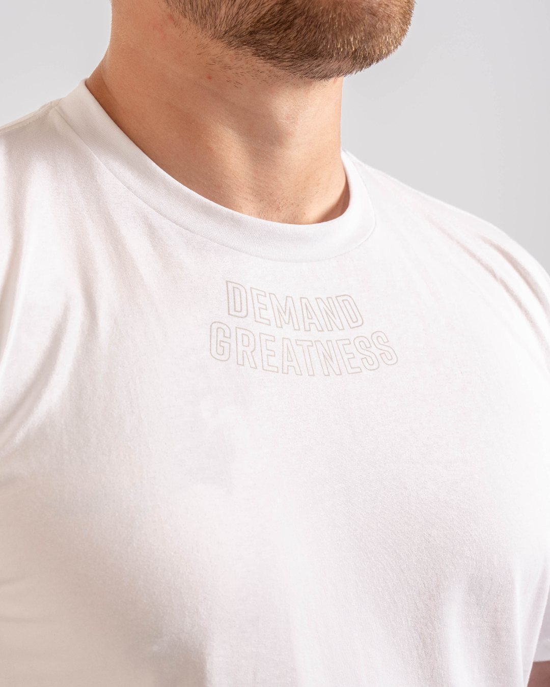 Close up of Demand Greatness text on the top of the chest on the front of the meet shirt