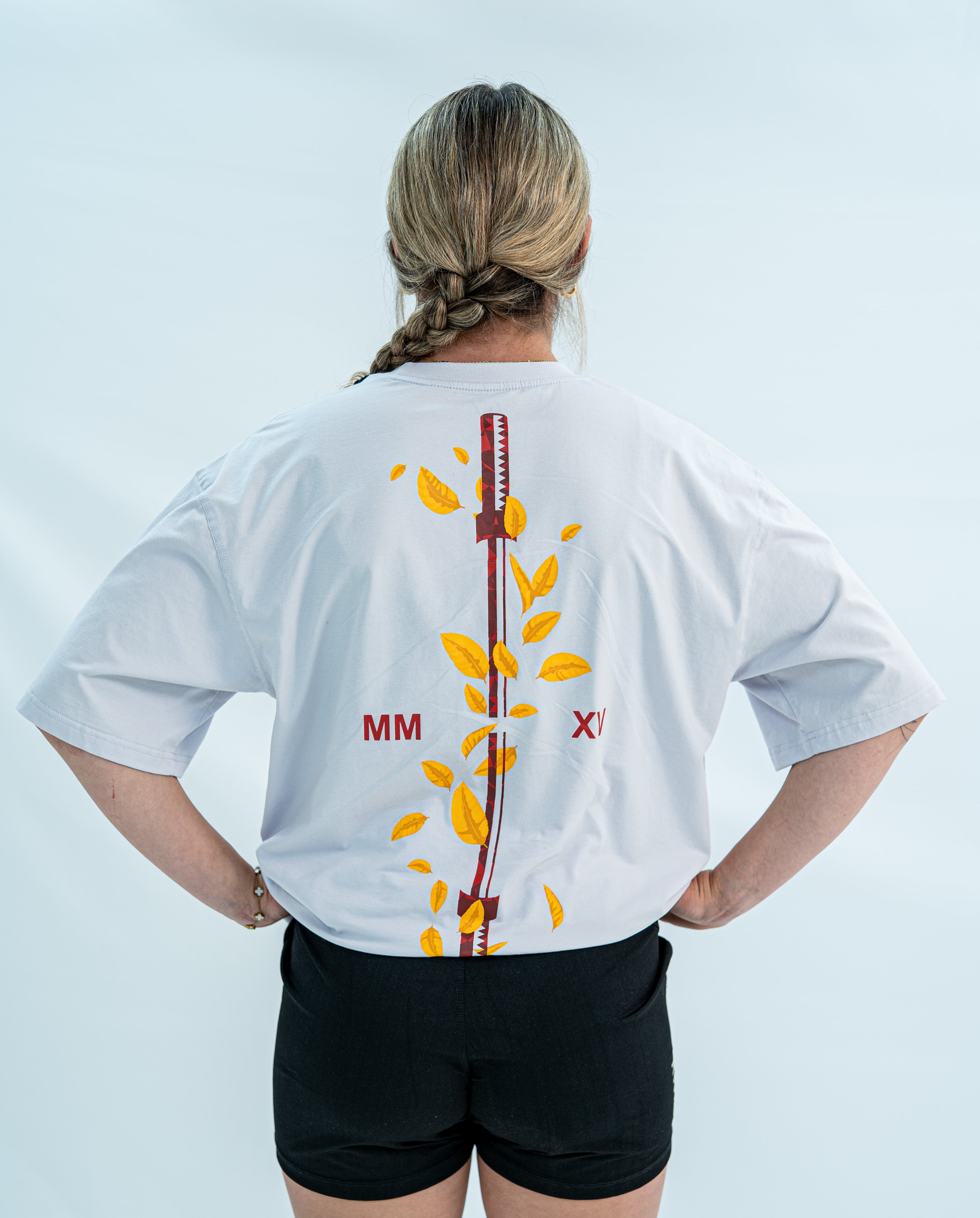 Female wearing a white over-fit shirt with a design on the back against a light gray background