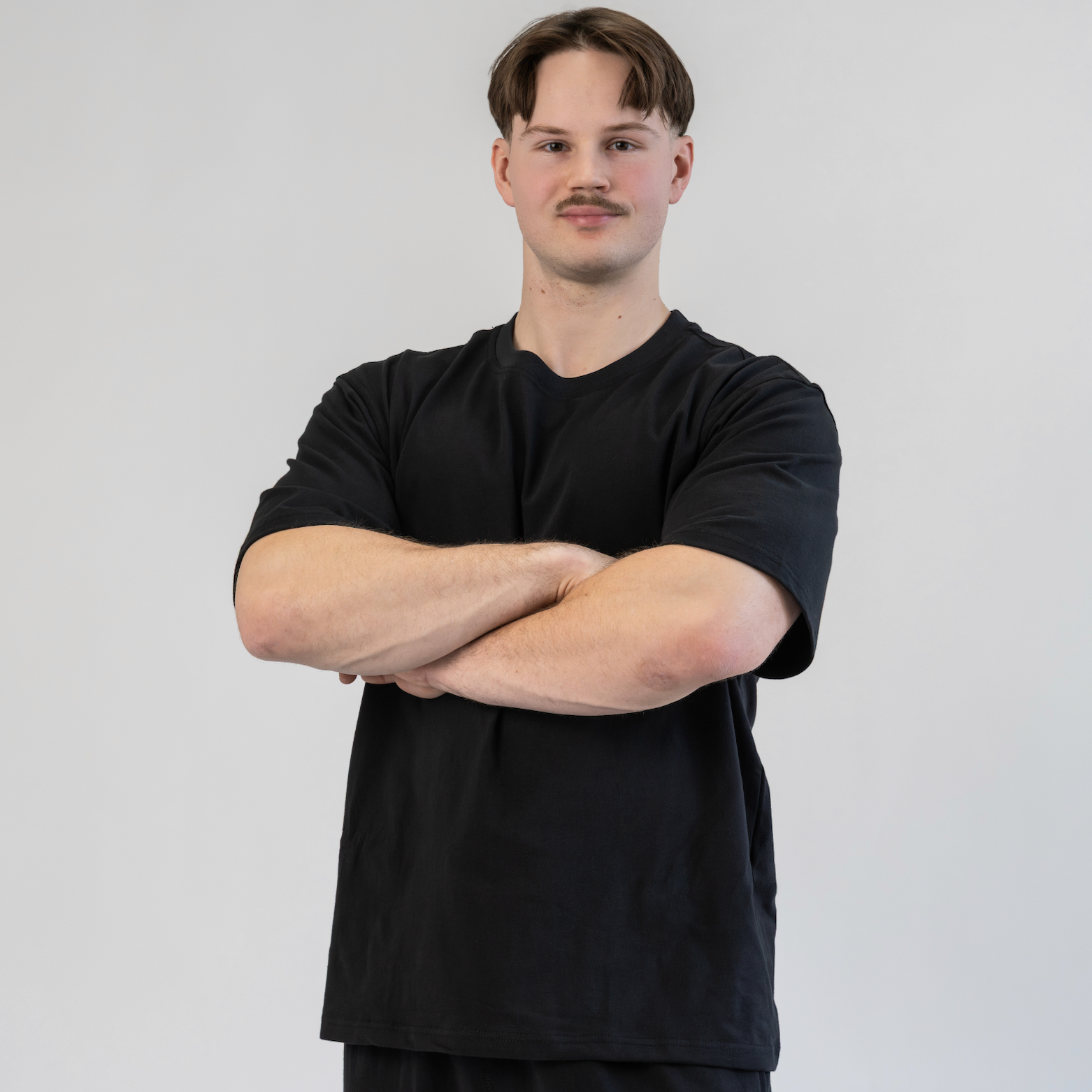 Man wearing a black t-shirt and dark pants against a plain background