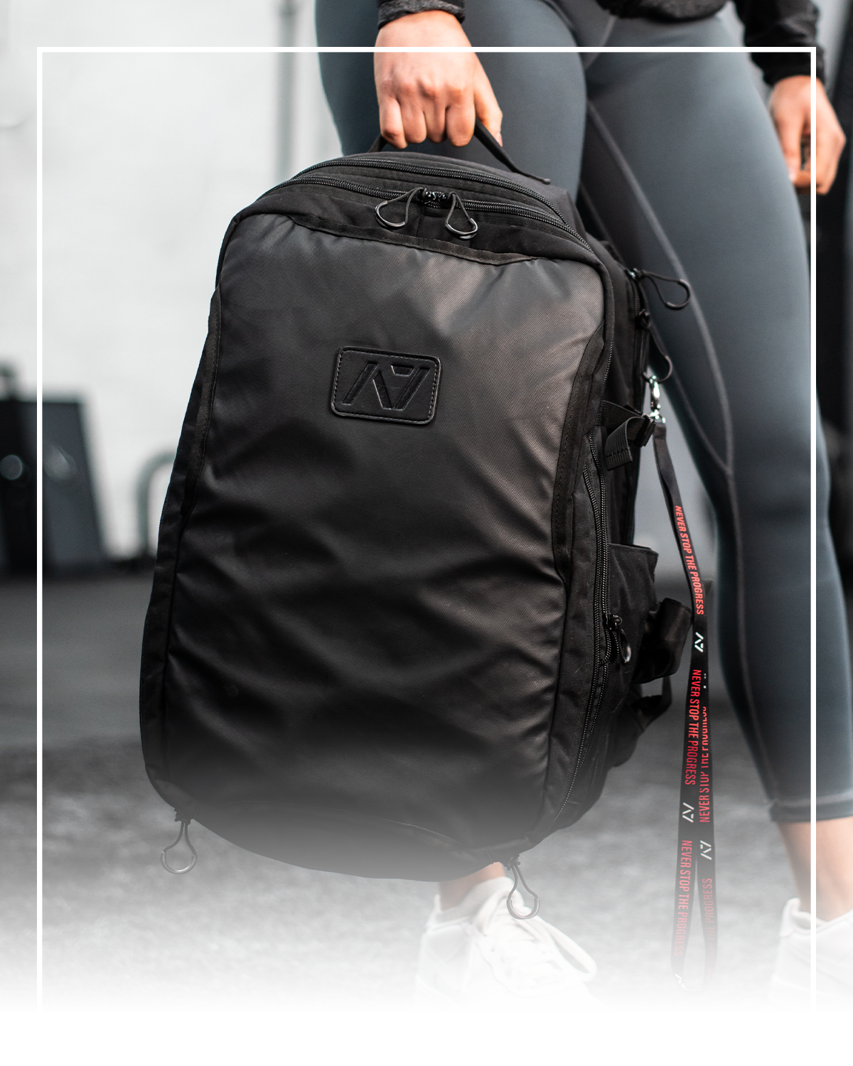 Black backpack with a brand logo held by a person wearing gray leggings.