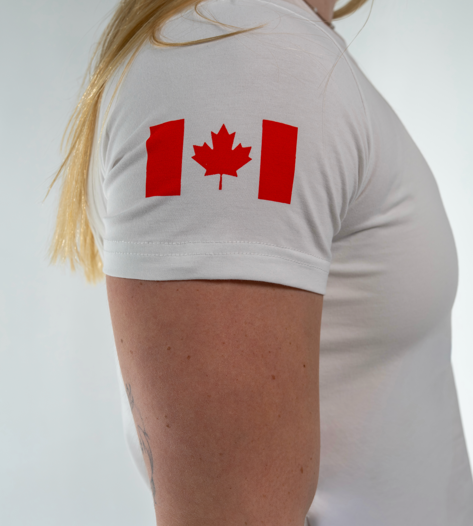 Person wearing a white t-shirt with a red maple leaf design on a plain background