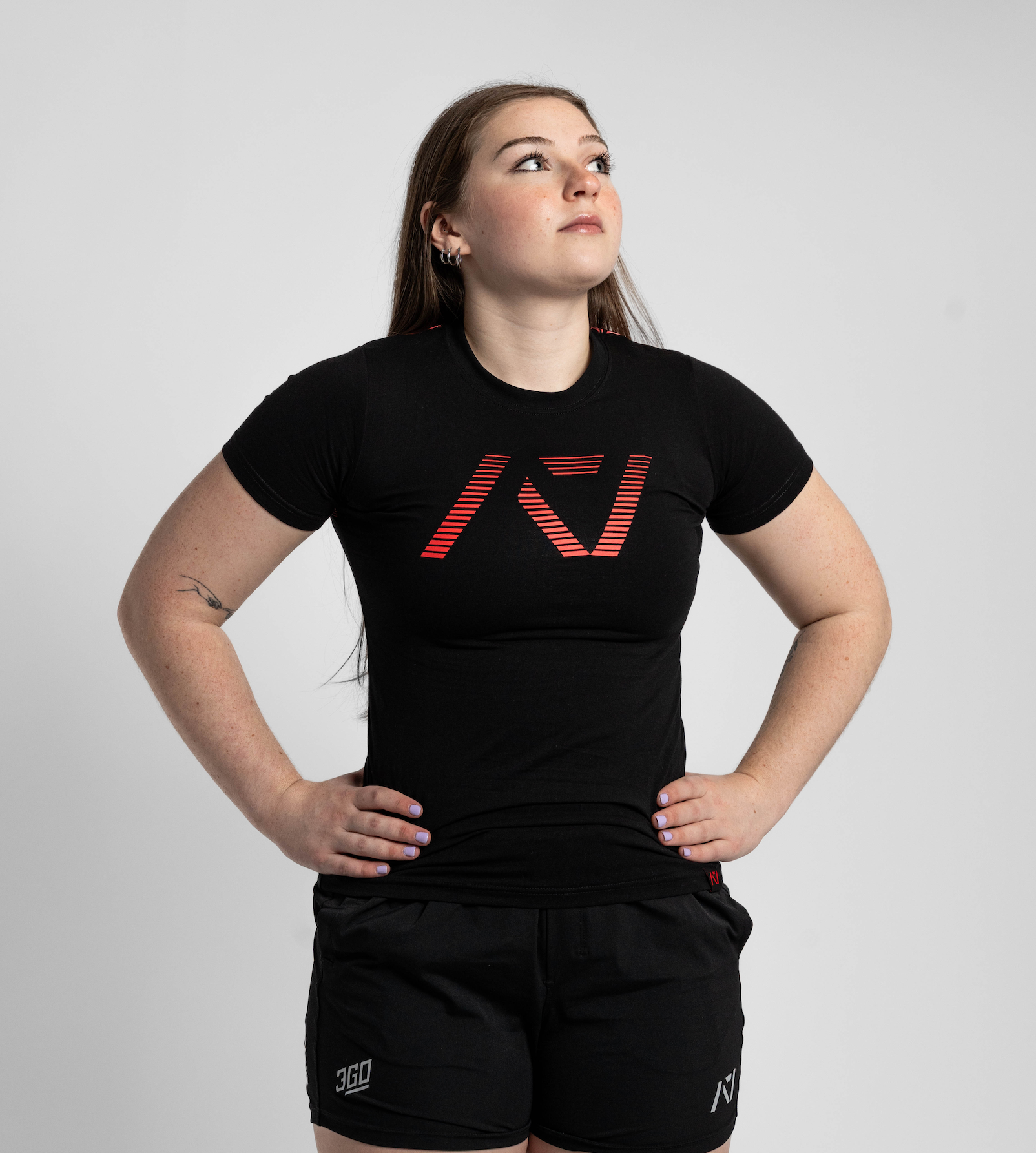 Person wearing a black t-shirt with a logo and black shorts on a light gray background