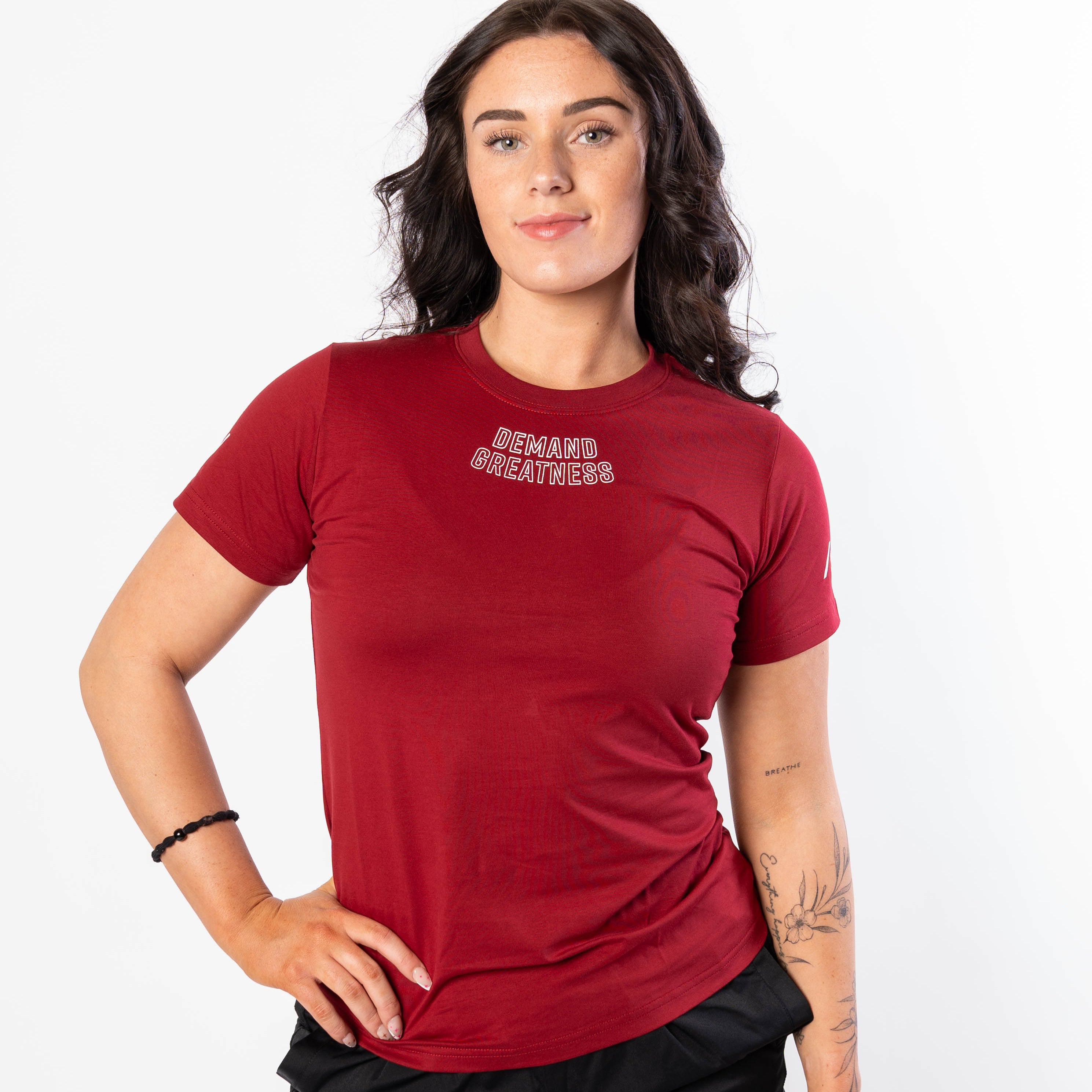 A woman wearing a red Demand Greatness True-Fit women's meet shirt with a logo on the upper chest and upper back.