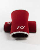 A pair of red knee sleeves with a white design that resembles a rose and tusk, symbolizing strength and beauty. The sleeves are designed with a hourglass-shaped center taper fit.
