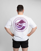Person wearing a white t-shirt with a purple logo on the back, standing against a plain background