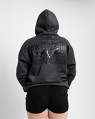 Person wearing a dark gray hoodie with branding on the back against a light gray background