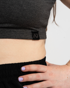Person wearing a dark gray crop top with a brand logo, black shorts.