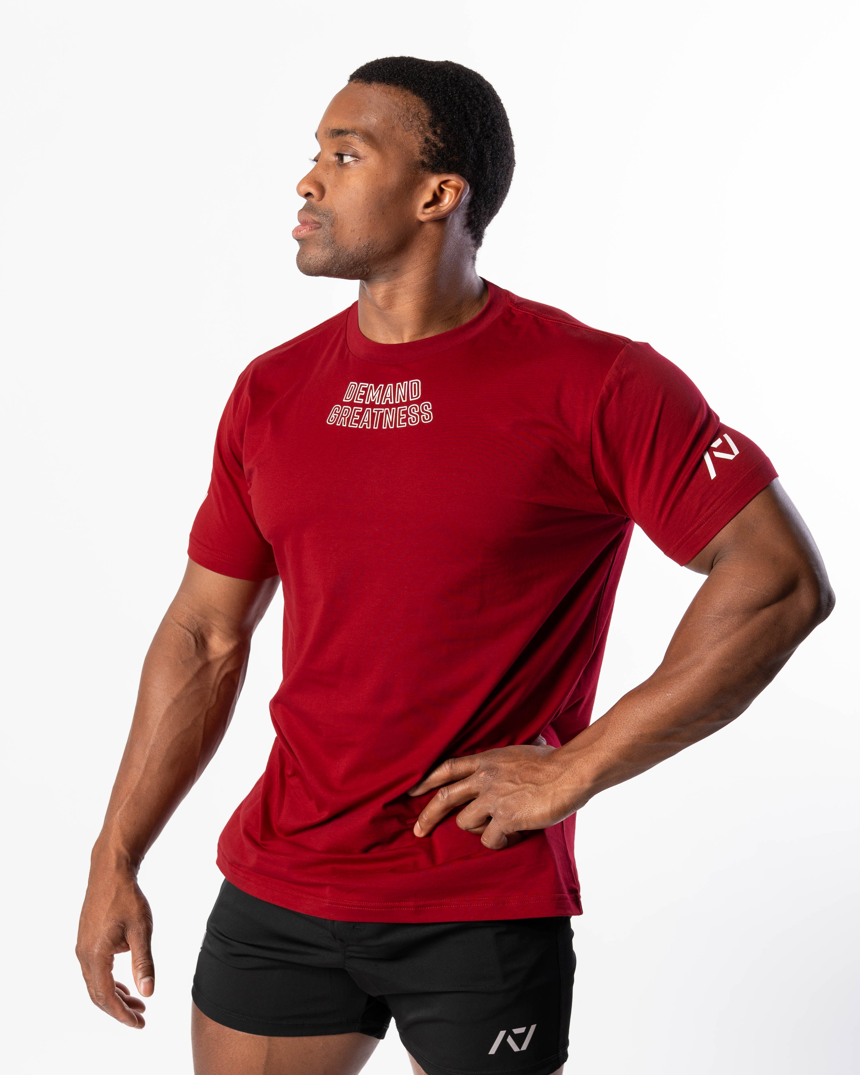 A man wearing a red Demand Greatness True-Fit men's meet shirt with a design on the upper chest and logos on the upper back and sleeves.